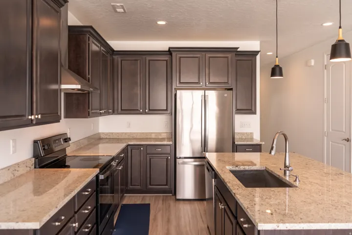 Kitchen featuring dark wood cabinetry, light-toned countertops, stainless steel appliances, a kitchen island with an undermount sink, and wood-finish flooring