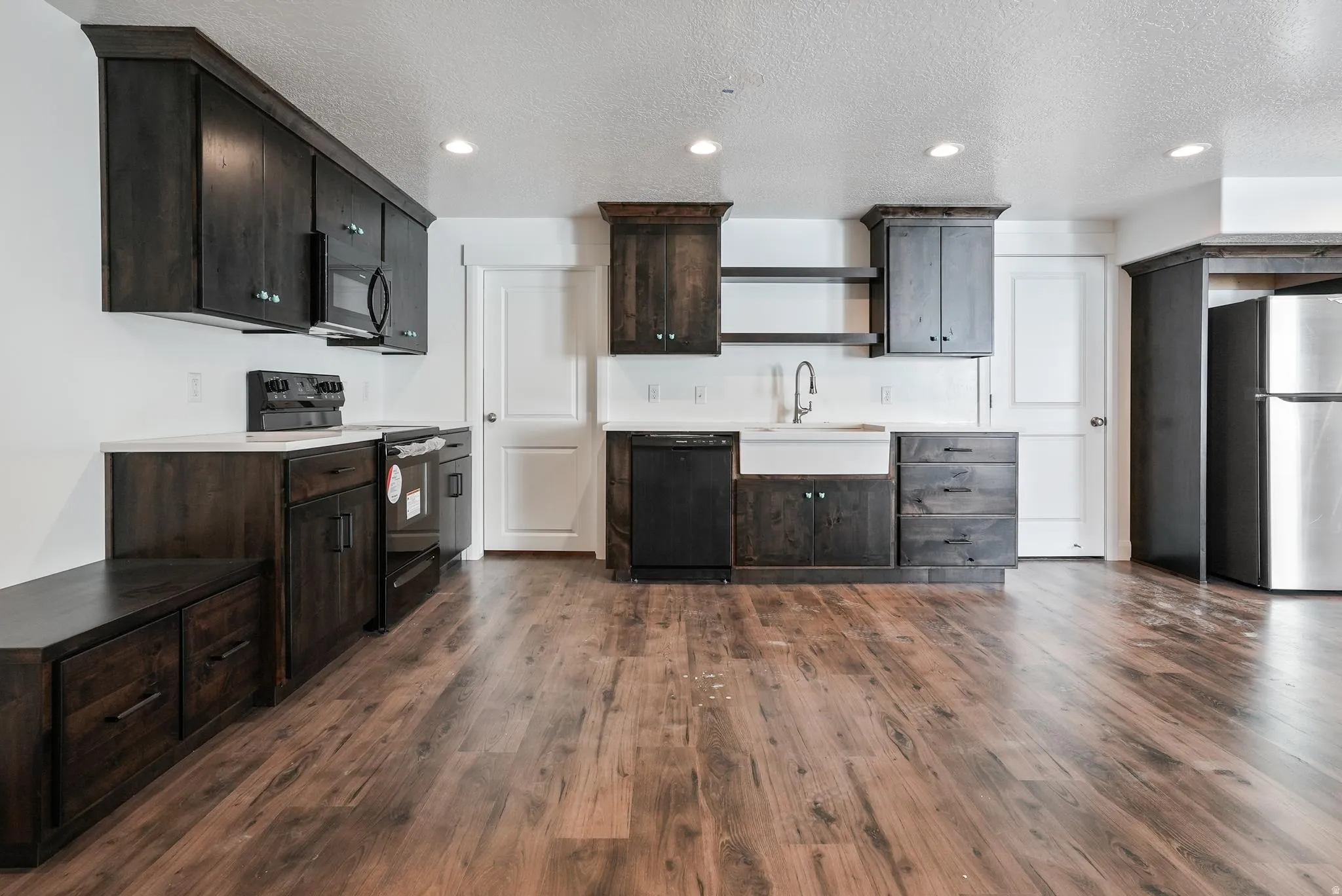 Kitchen featuring dark wood-finish cabinetry, stainless steel appliances, a farmhouse sink, and wood-finish flooring
