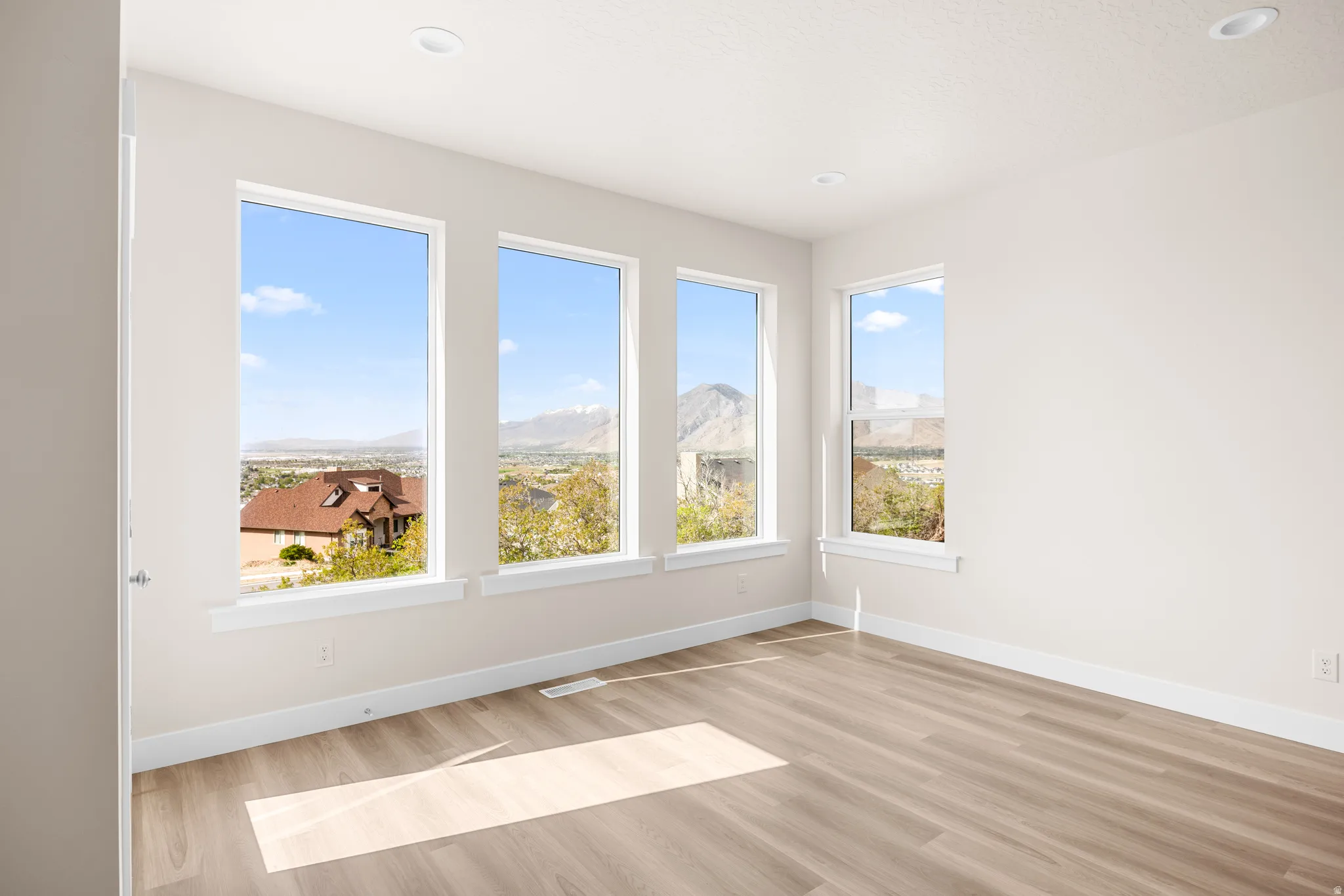 Expansive room featuring multiple large windows, recessed ceiling lighting, and wood-finish flooring
