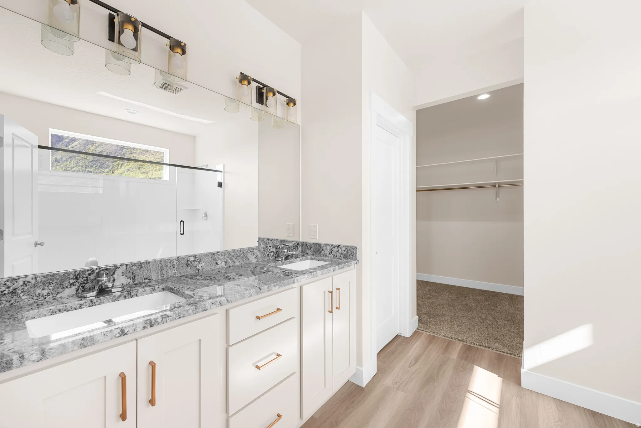 Dual vanity with undermount sinks, granite countertops, and white shaker-style cabinetry with copper-finish hardware
