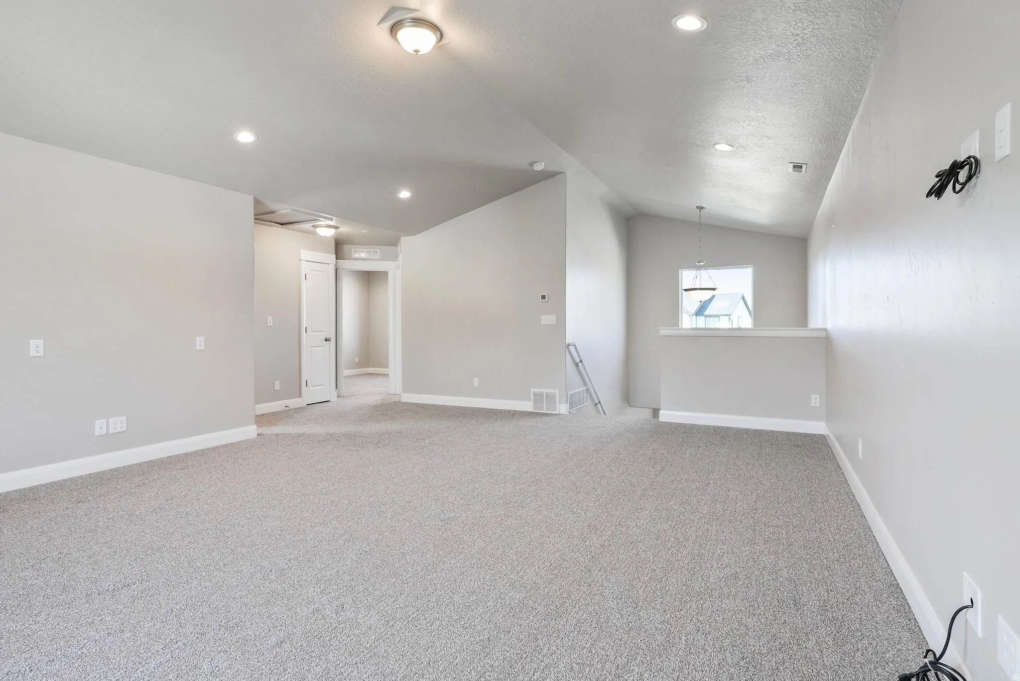 Spacious carpeted area with recessed lighting, vaulted ceilings, and a half-wall partition featuring a window