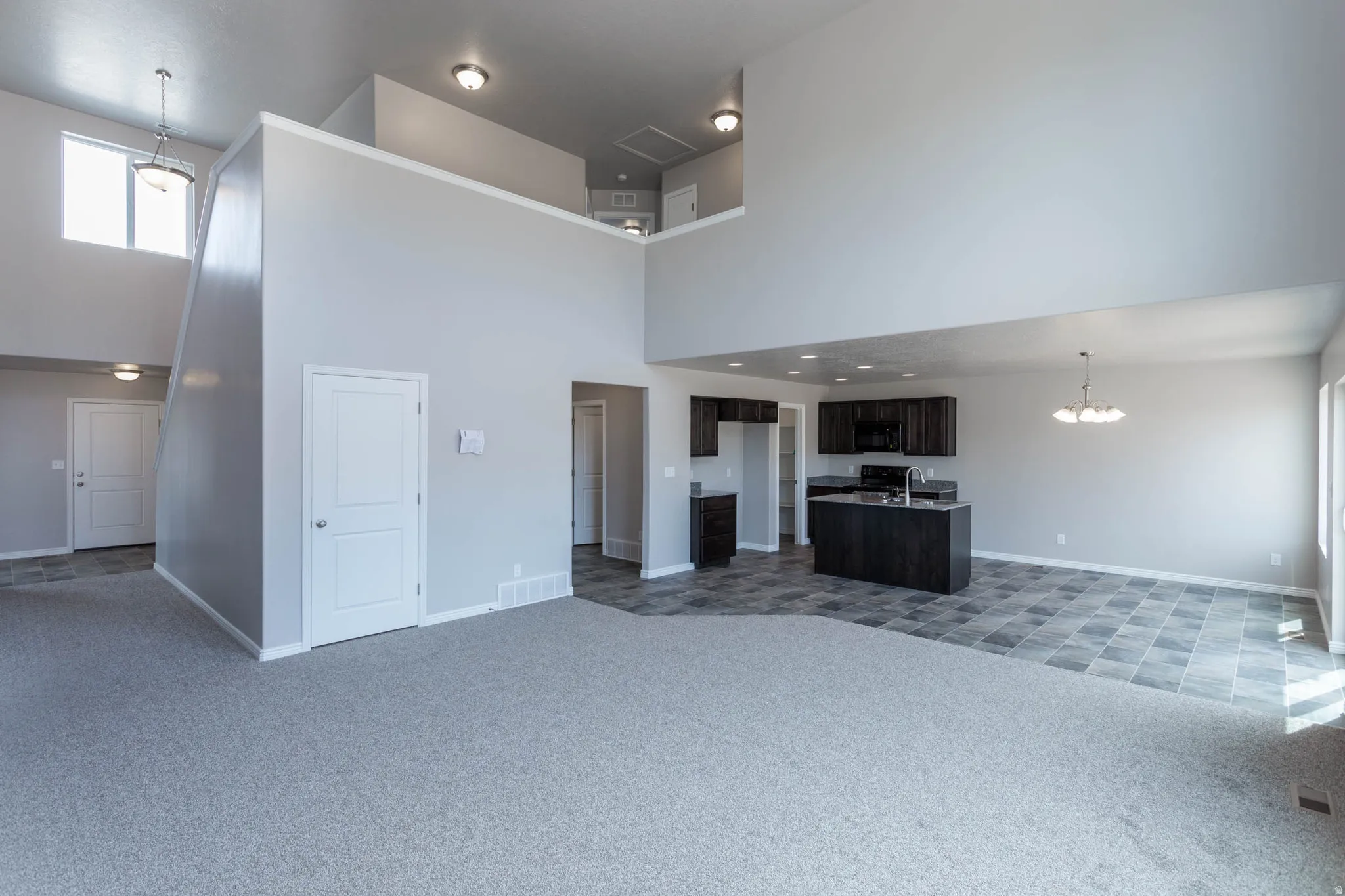 Open-concept living space with high ceilings, carpeted flooring, and an elevated second-story landing