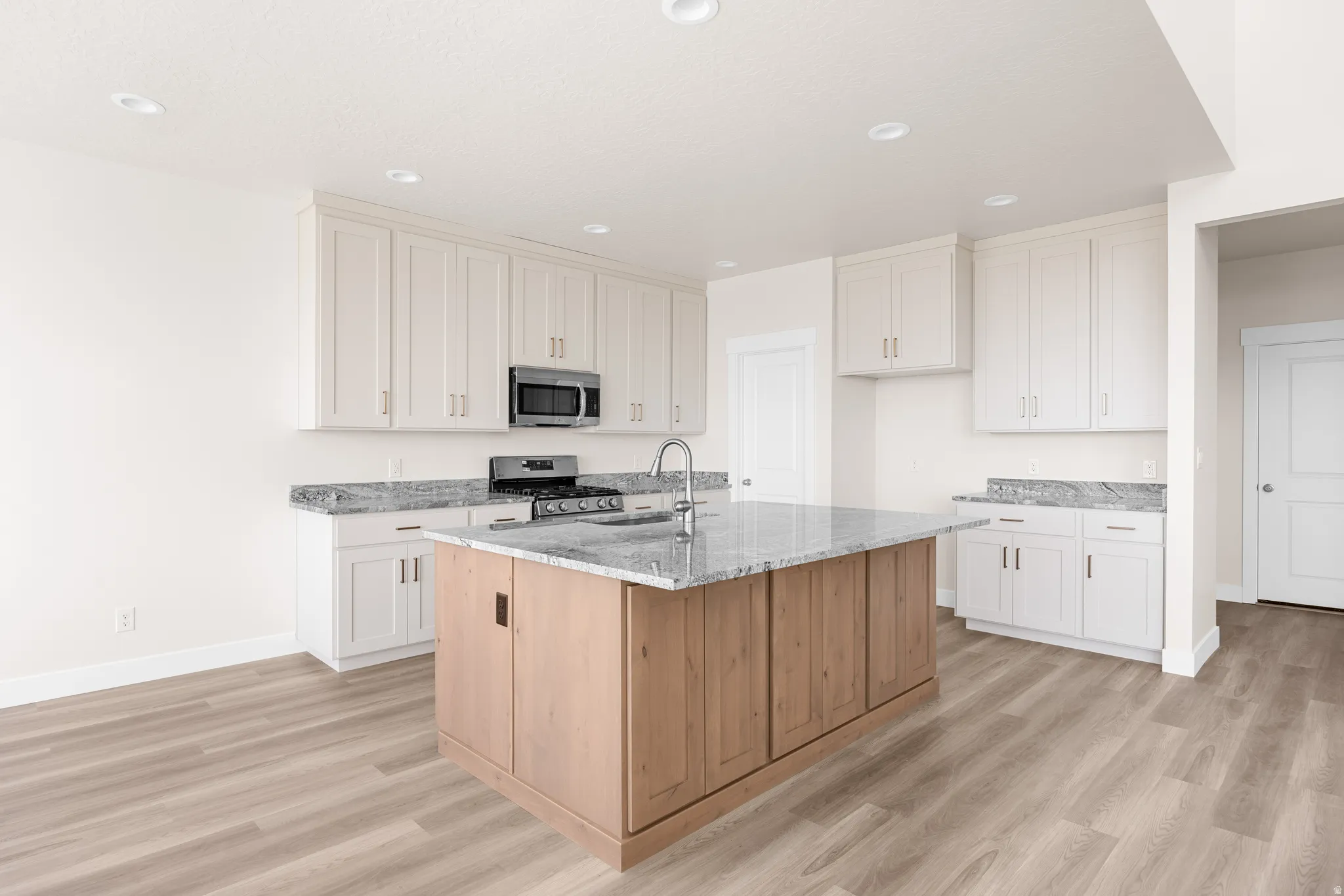 Kitchen featuring a wood-finish island, white cabinetry, integrated stainless steel appliances, granite countertops, and wood-finish flooring