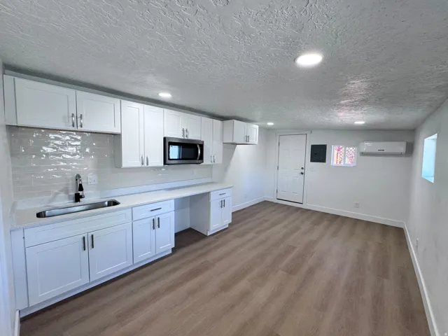 Wood-finish flooring, recessed lighting, white cabinetry with modern hardware, integrated microwave, and a stainless steel sink with a matte black faucet