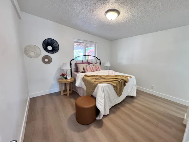 Window with exterior landscaping, wood-finish flooring, white walls, and a ceiling-mounted light fixture