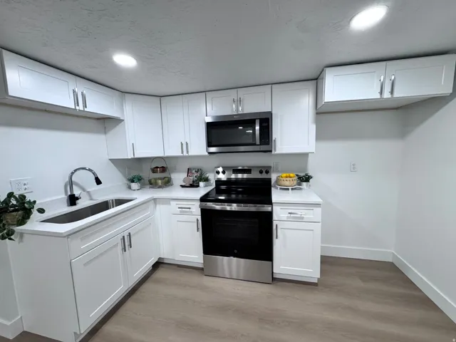 White shaker cabinetry, stainless steel appliances, undermount sink with a gooseneck faucet, light-toned wood-finish flooring, and recessed lighting