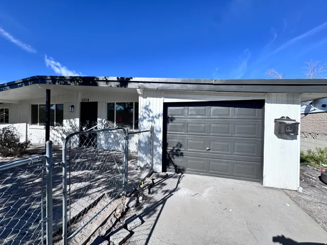 White exterior siding and brick accents with an attached garage, covered entryway, and chain-link fencing