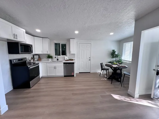 White shaker cabinetry, stainless steel appliances, wood-finish flooring, recessed lighting, and a window with blinds