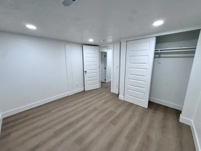 Recessed lighting illuminates the room, featuring wood-finish flooring, white walls, and a sliding closet door