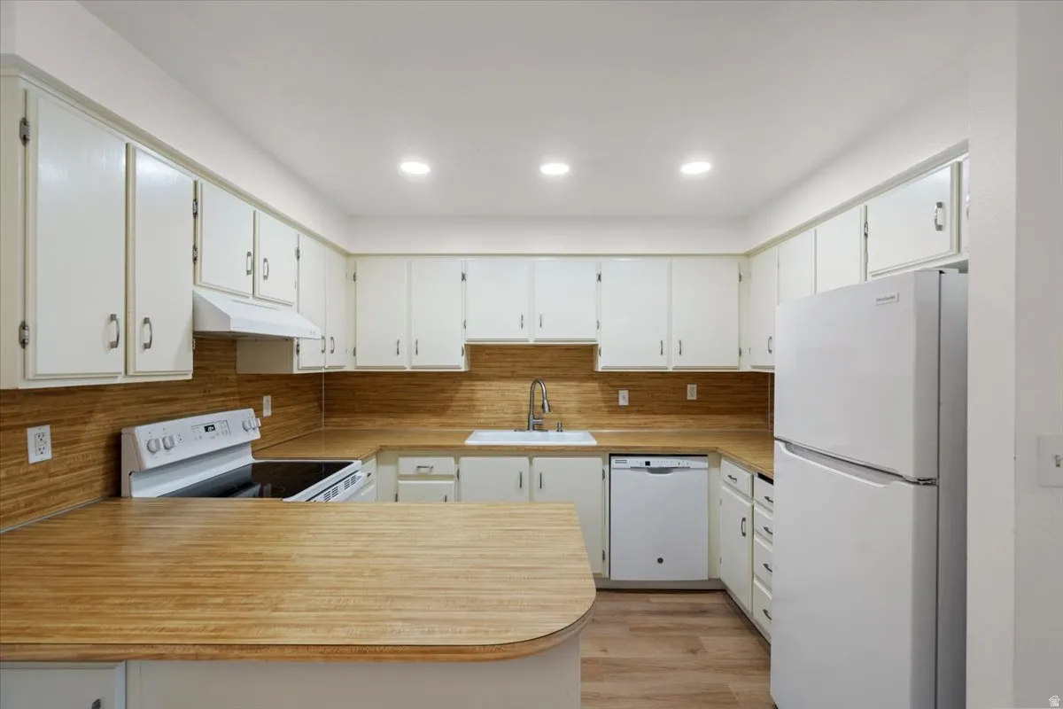 Kitchen featuring white cabinetry, wood-finish countertops, wood-finish flooring, recessed lighting, and white appliances
