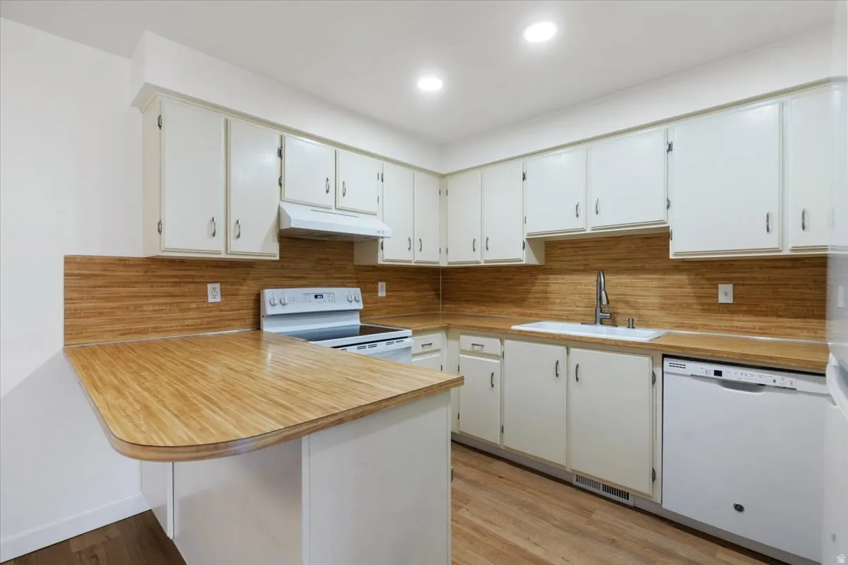 Kitchen featuring white cabinetry, wood-finish countertops, wood-finish flooring, white electric range, and a white dishwasher