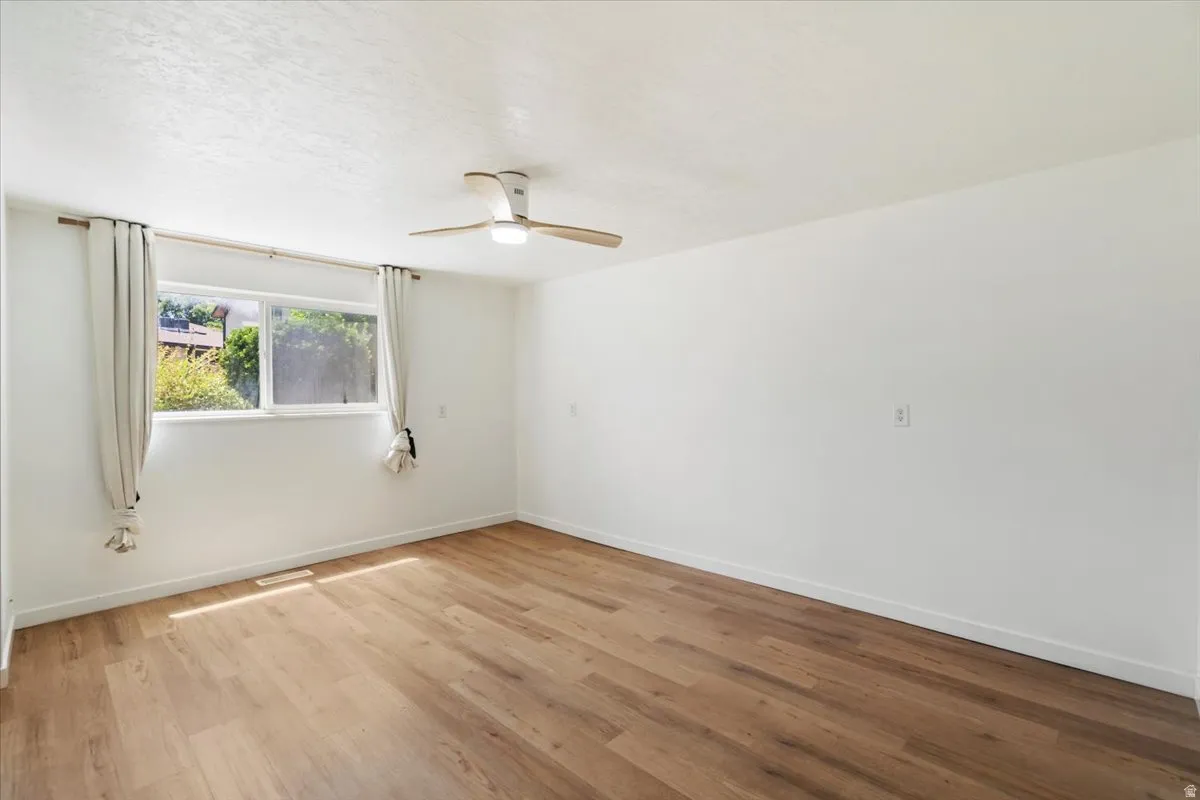 Wood-finish flooring, white walls, and a ceiling-mounted fan with integrated lighting