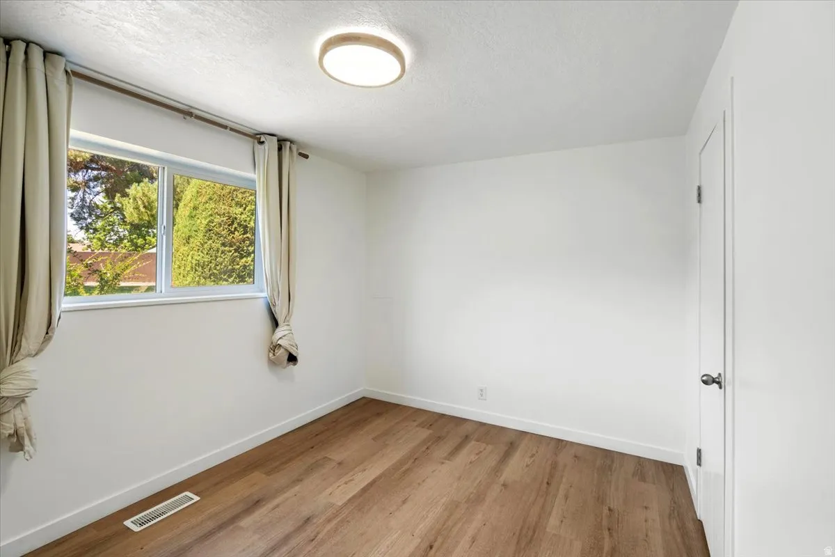 Wood-finish flooring, white walls, flush mount ceiling light, and a white door with dark hardware