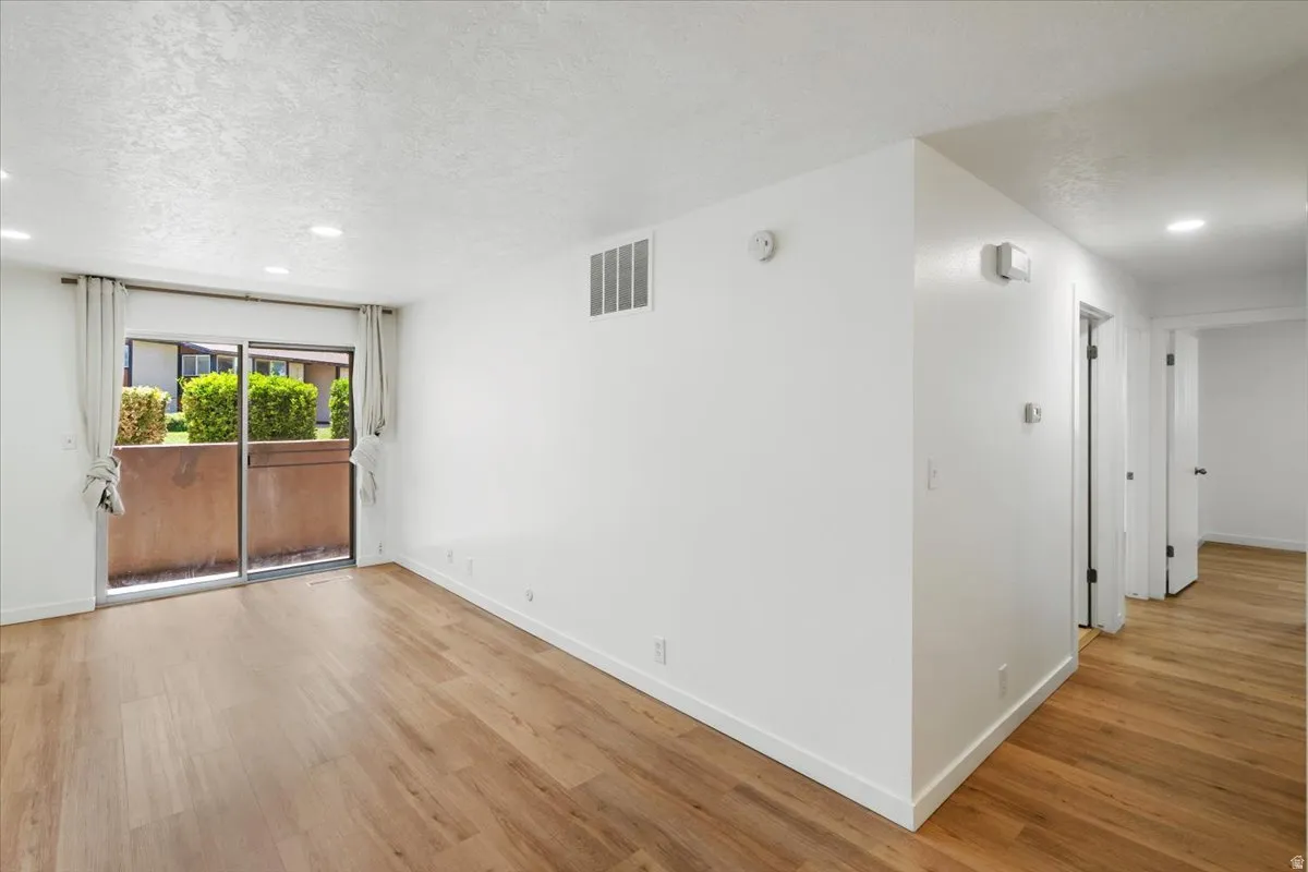 Wood-finish flooring, recessed ceiling lighting, sliding glass door, and a white interior palette