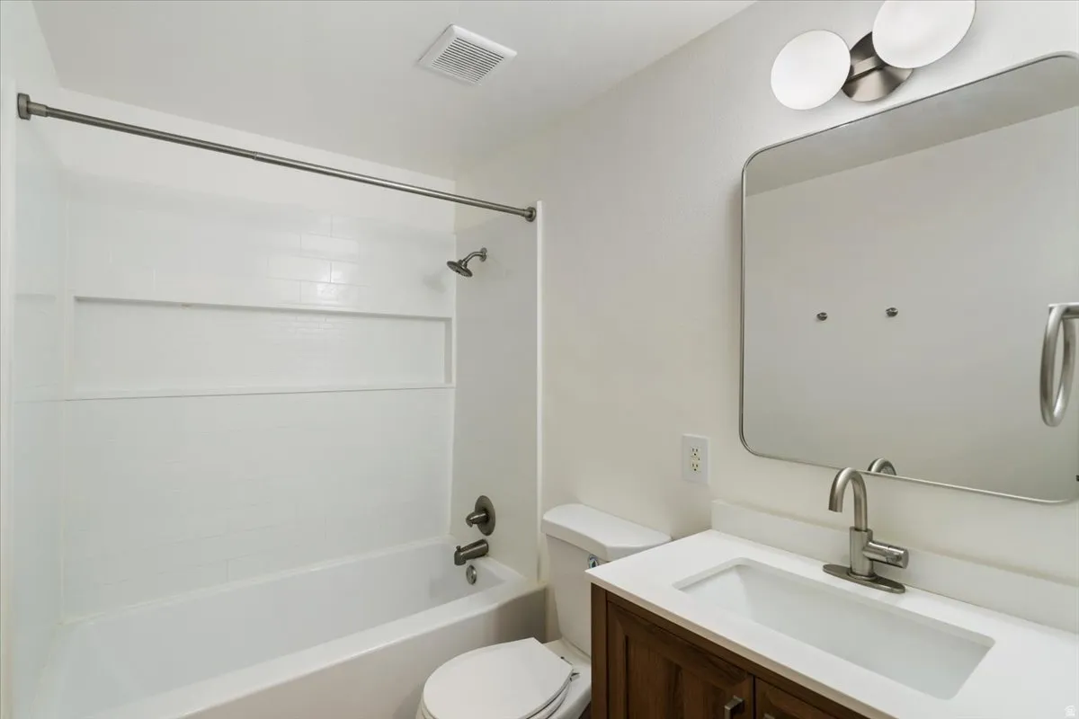 Bathroom featuring a tub/shower combination, white vanity countertop, wood-finish vanity, and wall-mounted mirror with integrated lighting