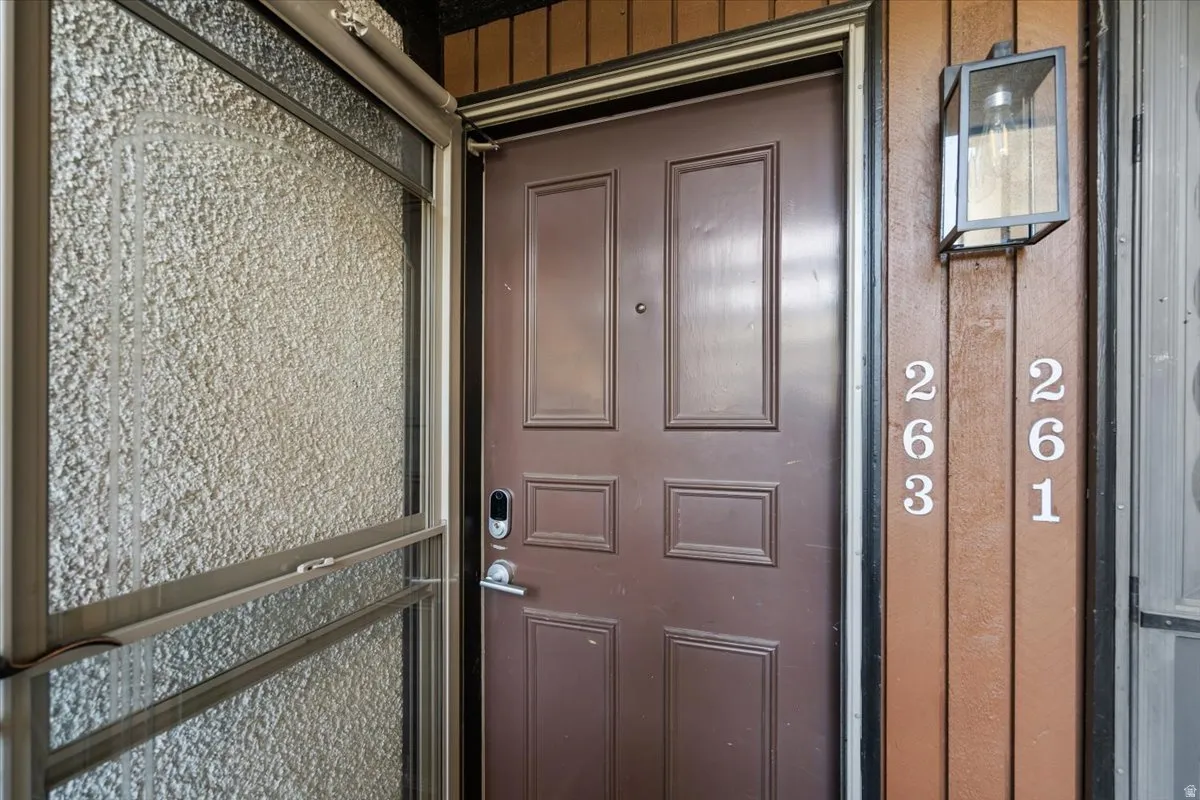 Brown paneled entry door with smart lock, accompanied by an exterior wall sconce