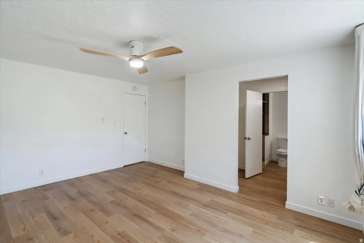 Wood-finish flooring, white painted walls, and a modern ceiling fan with integrated lighting