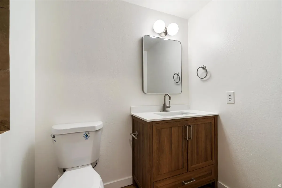 White toilet, wood-finish vanity with built-in sink, white countertop, and brushed nickel hardware