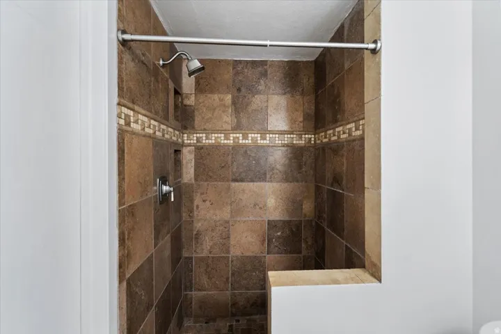 Tiled shower with a decorative mosaic accent band, recessed shelf, and built-in bench