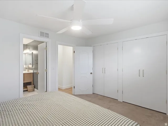 White ceiling fan with integrated lighting, multiple white closet doors with brushed nickel pulls, neutral carpeting, and a white interior door