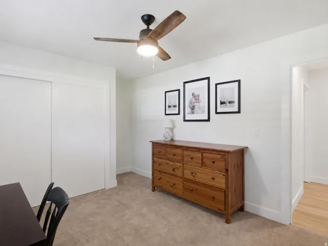 Neutral wall paint, ceiling fan with wood-finish blades, soft carpet flooring, and a sliding door closet