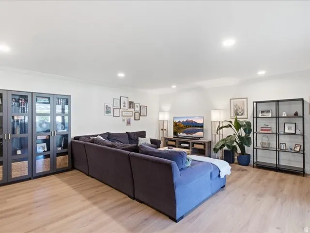 Recessed lighting, crown molding, wood-finish flooring, built-in display cabinetry, and a wall-mounted television