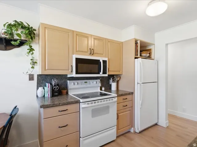 Light wood-finish cabinetry with black hardware, dark speckled countertops, white appliances, and wood-finish flooring