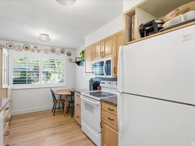 Kitchen featuring wood-finish flooring, white appliances, wood cabinetry, and a double window with plantation shutters