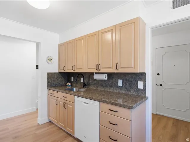 Light wood-finish cabinetry, dark speckled countertops, stainless steel sink with matte black faucet, integrated dishwasher, and light wood-finish flooring
