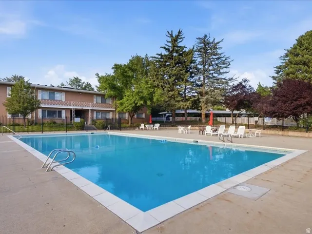 Expansive outdoor swimming pool with concrete surround, featuring perimeter fencing and mature landscaping