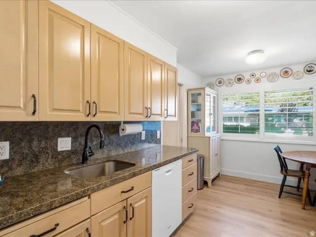 Kitchen featuring wood-finish flooring, light wood cabinetry with dark hardware, stone-look countertops, and a white dishwasher
