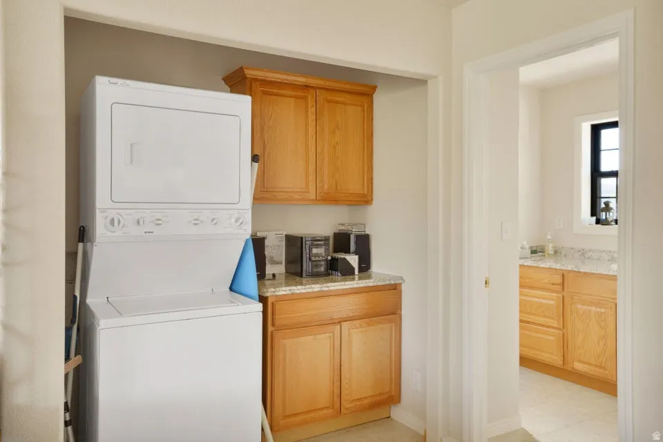 Stackable washer and dryer, light wood-finish cabinetry, light-toned countertop, and recessed lighting