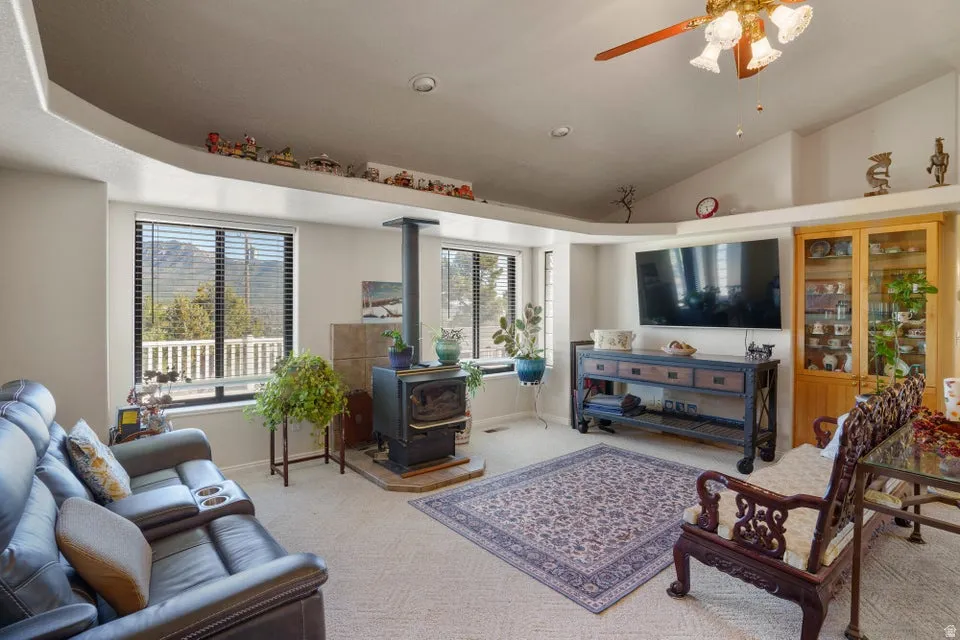 Vaulted ceiling with a ceiling fan and recessed lighting, bay windows with mountain scenery, wood-burning stove with a tiled hearth, and an integrated display shelf
