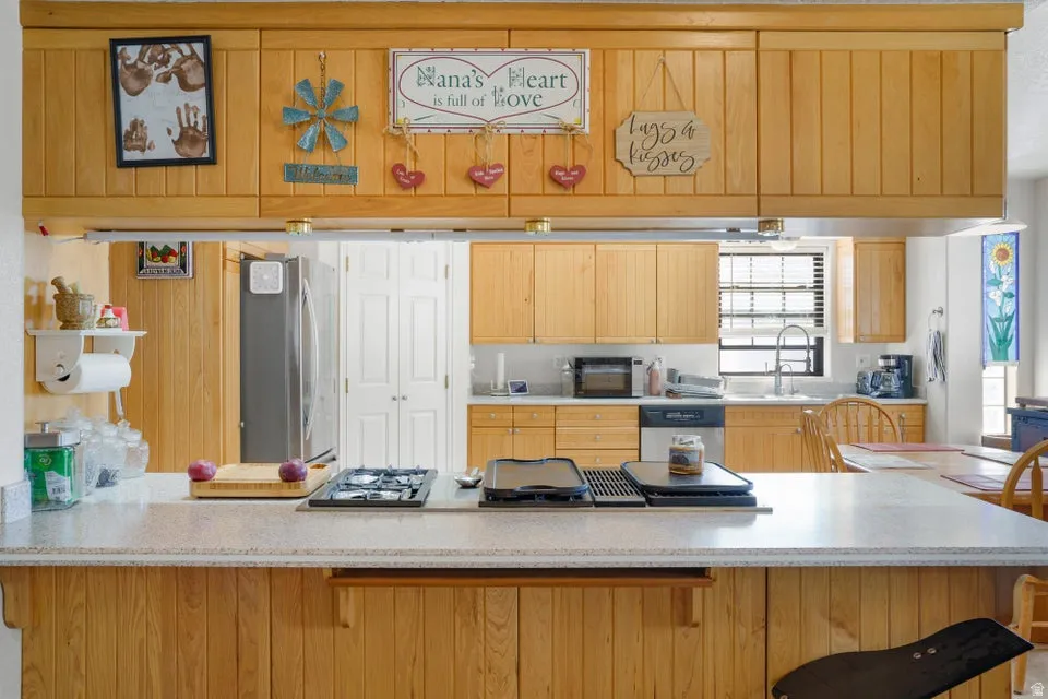 Kitchen featuring wood cabinetry, stainless steel refrigerator, integrated cooktop, dishwasher, and a window with blinds
