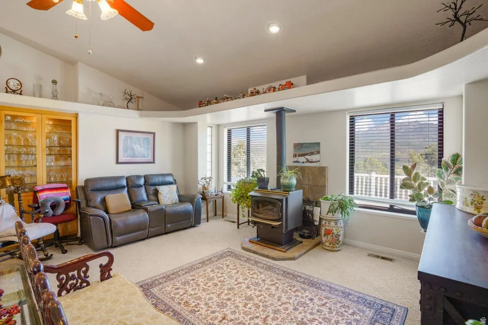 Vaulted ceiling with recessed lighting and ceiling fan, wood-burning stove with stone hearth, built-in display shelving, and light wood-finish built-in cabinetry