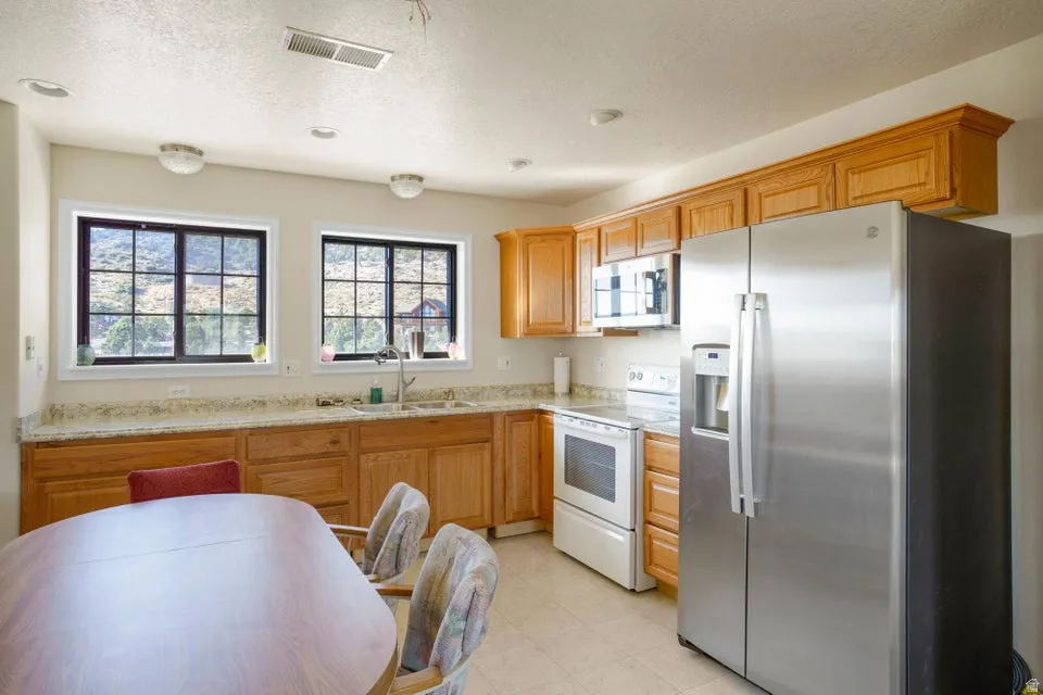 Kitchen featuring light wood cabinetry, light-toned countertops, two grid-pattern windows, and a stainless steel refrigerator