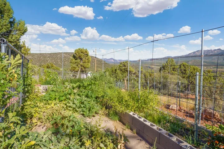 Terraced garden beds featuring established plantings and a perimeter fence, set against a backdrop of distant mountains