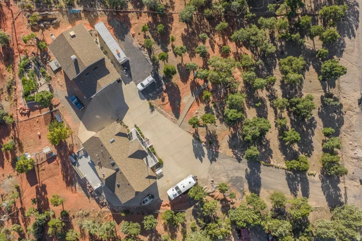 Expansive property featuring two structures with shingle roofing, extensive paved driveways, and natural arid landscaping with mature trees