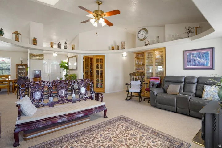 Vaulted ceilings with a ceiling fan, illuminated display ledges, and built-in cabinetry with glass doors