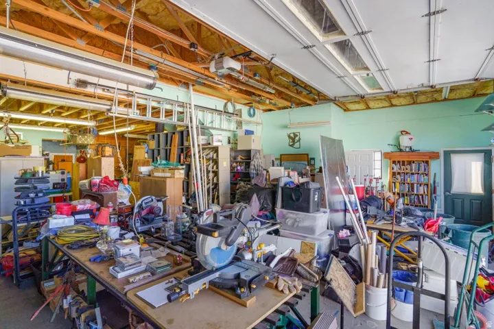 Exposed wood beam ceiling, multiple fluorescent light fixtures, two overhead garage doors, painted walls, interior doors with trim