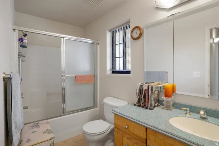 Bathtub with sliding glass enclosure, single vanity with integrated sink, wood-finish cabinetry, and mirrored medicine cabinet