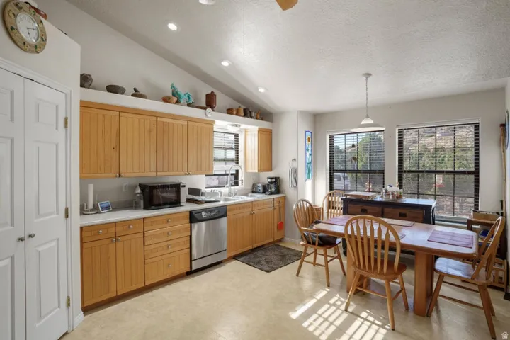 Vaulted ceiling with recessed lighting, light wood-finish cabinetry, stainless steel dishwasher, white countertops, and dual windows