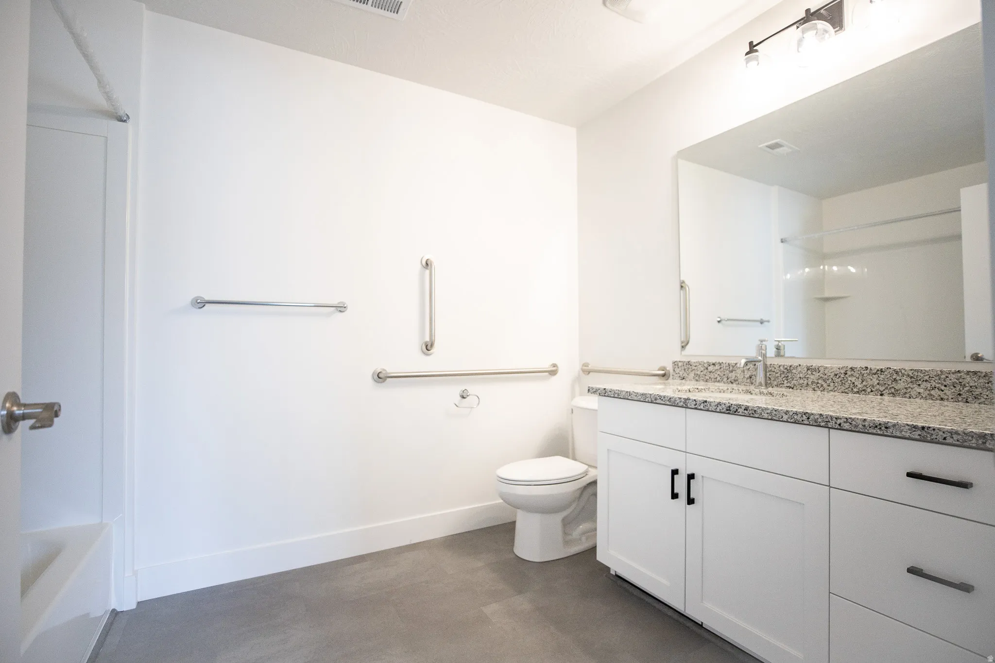 Large ADA accessible secondary bath with grab bars, painted white wood cabinets and granite countertops.