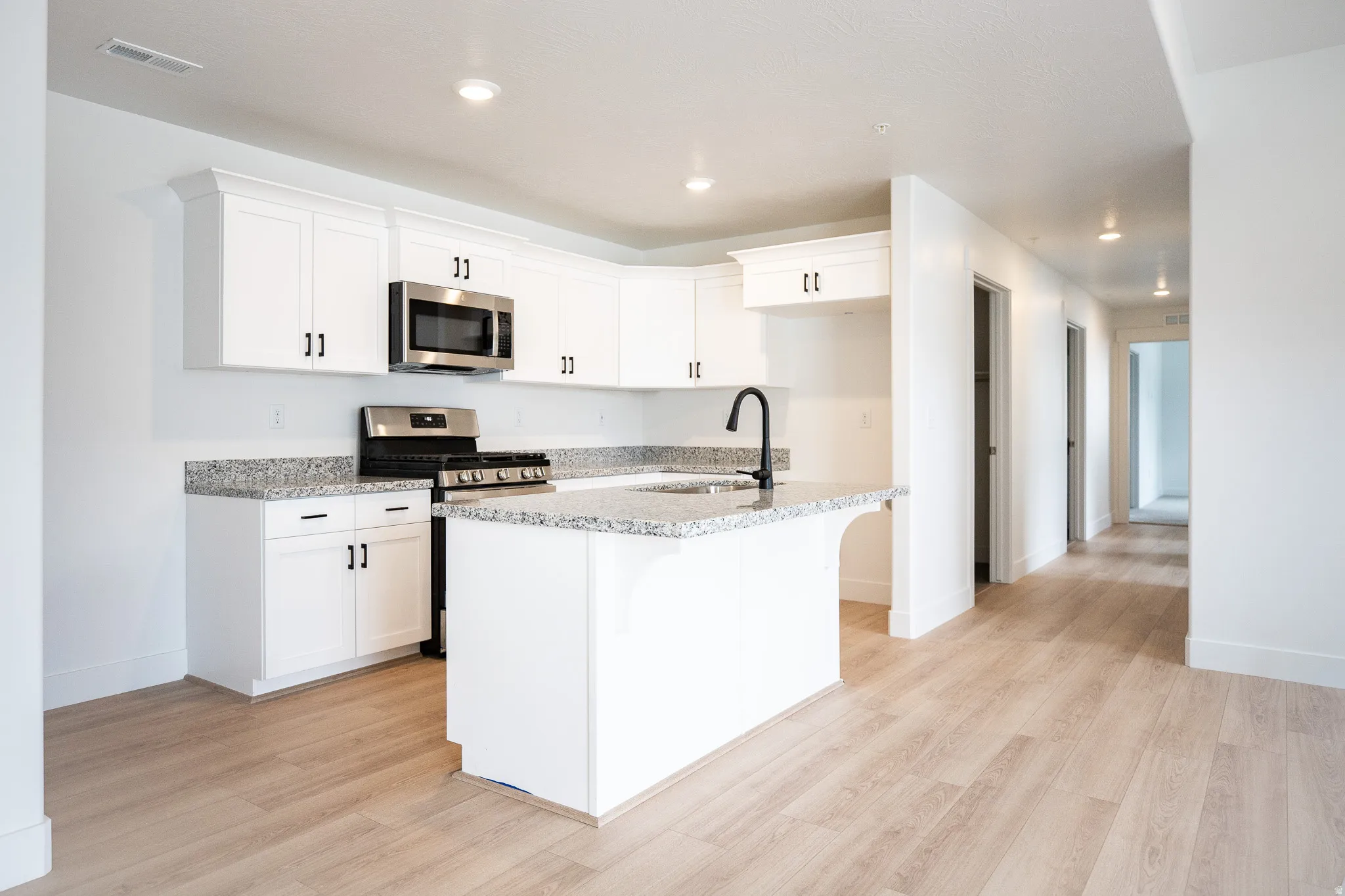 Terrific ADA accessible kitchen with painted white wood cabinets, granite slab counters, gas range, microwave, built-in dishwasher and disposal.