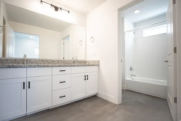 Primary ADA accessible bathroom with grab bars, dual sinks, painted white wood cabinets and granite counters.