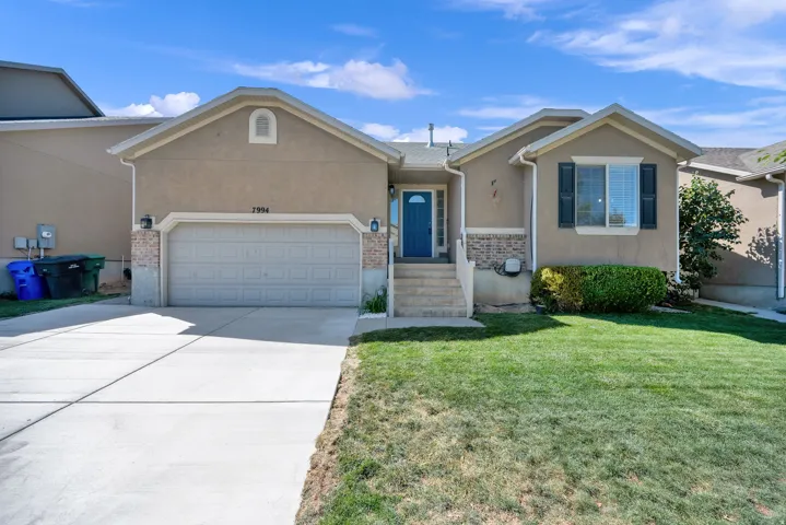 Stucco exterior with brick accents, attached garage, concrete driveway, front entry steps, and a blue front door