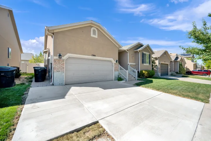 Stucco exterior with brick accents, attached garage, concrete driveway, and established landscaping