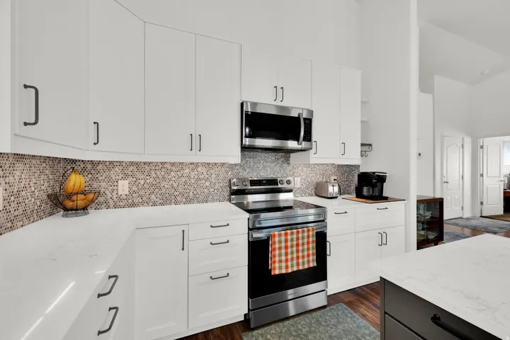 White cabinetry with matte black hardware, stainless steel appliances, mosaic tile backsplash, light-toned countertop, and wood-finish flooring