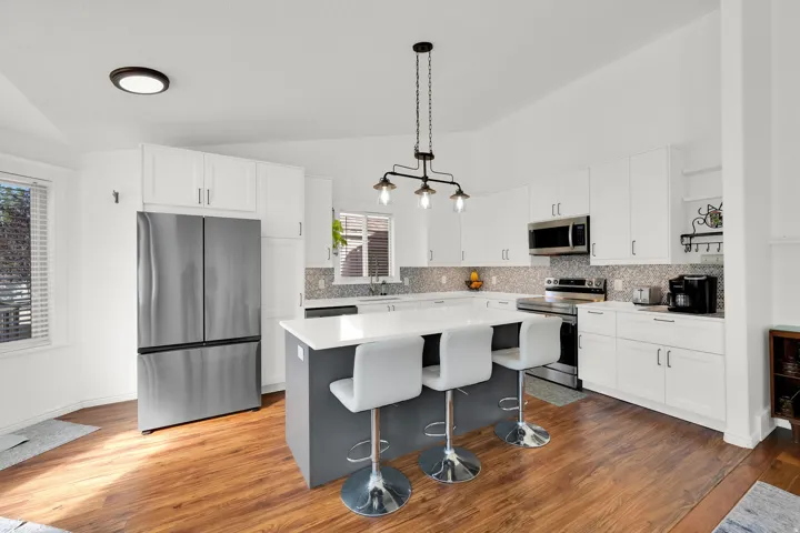 Kitchen featuring a center island, white cabinetry, stainless steel appliances, wood-finish flooring, and a mosaic tile backsplash
