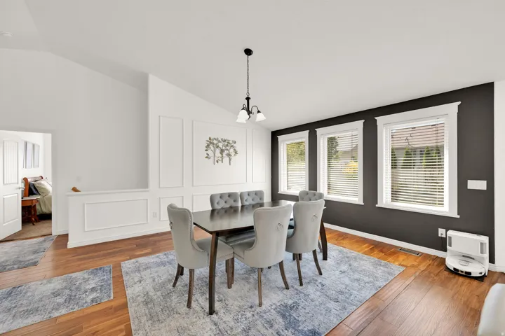 Vaulted ceilings with a pendant light fixture, wood-finish flooring, accent wall with three windows, and wainscoting detail